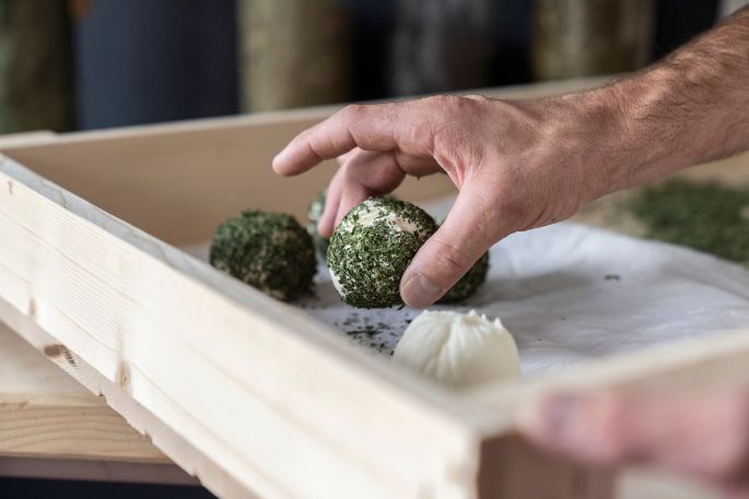 Der Käse wird von Hand mit Kräutern bestreut.